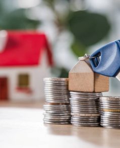 selective focus of key with toy house trinket on stacks of coins near house model on wooden table selective focus of key with toy house trinket on stacks of coins near house model on wooden table